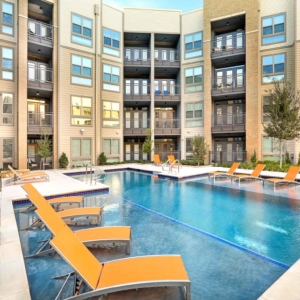 lap pool with tanning ledges filled with lounge furniture and the building facade in the background